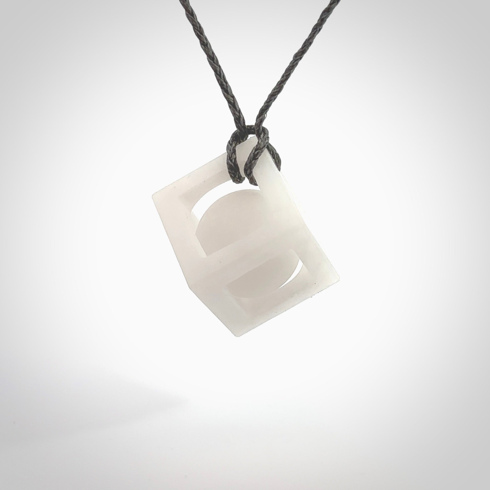 A hand carved medium sized white nephrite Jade square box with ball inside necklace. The cord is grey and adjustable in length. A medium sized hand made cube/box with ball necklace in white nephrite Jade stone. One off work of art to wear.