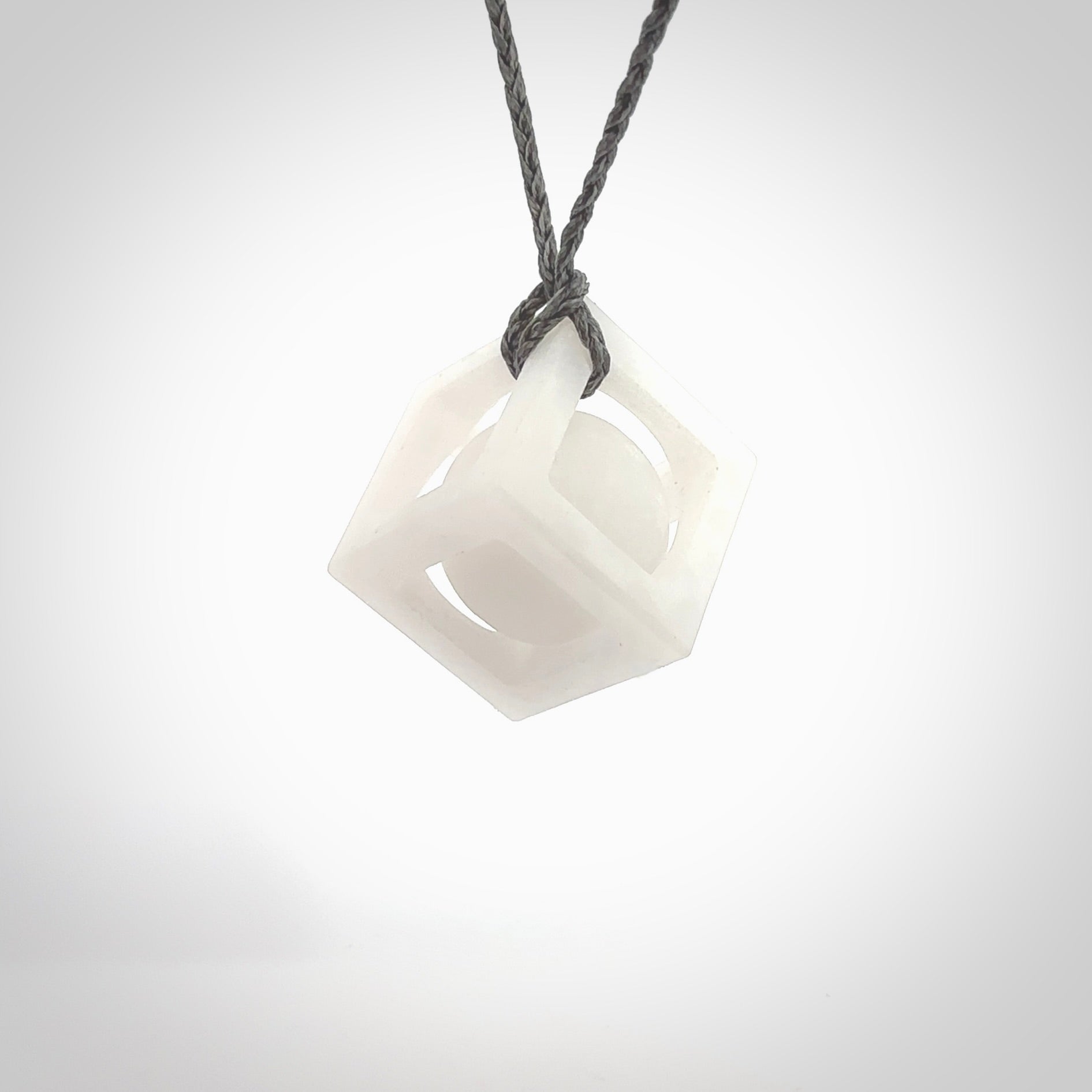 A hand carved medium sized white nephrite Jade square box with ball inside necklace. The cord is grey and adjustable in length. A medium sized hand made cube/box with ball necklace in white nephrite Jade stone. One off work of art to wear.