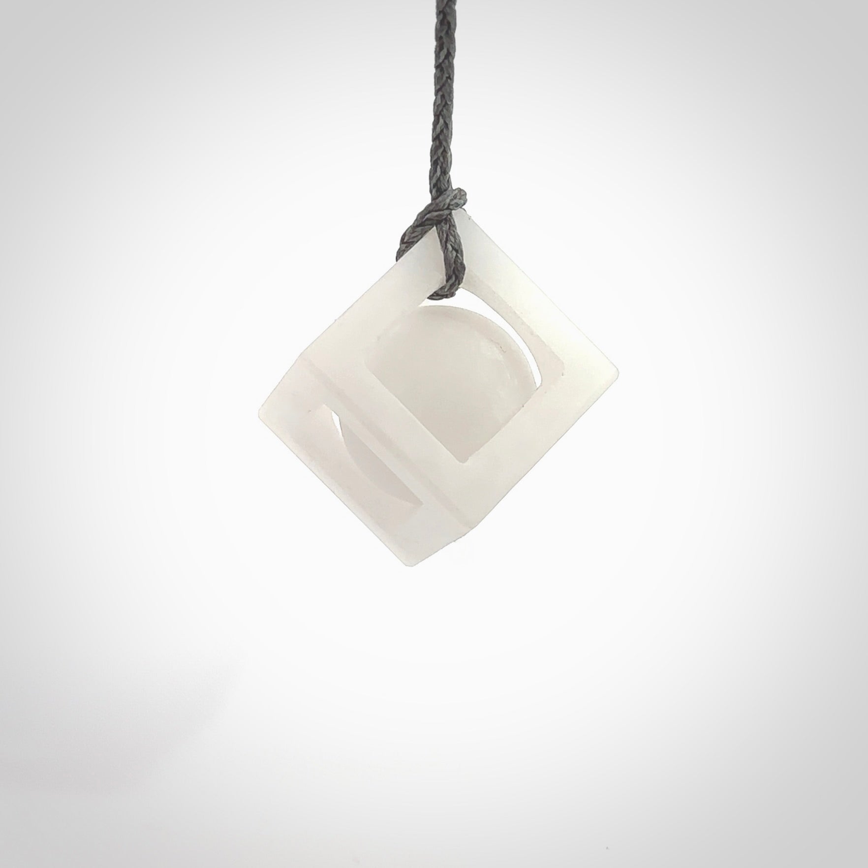 A hand carved medium sized white nephrite Jade square box with ball inside necklace. The cord is grey and adjustable in length. A medium sized hand made cube/box with ball necklace in white nephrite Jade stone. One off work of art to wear.