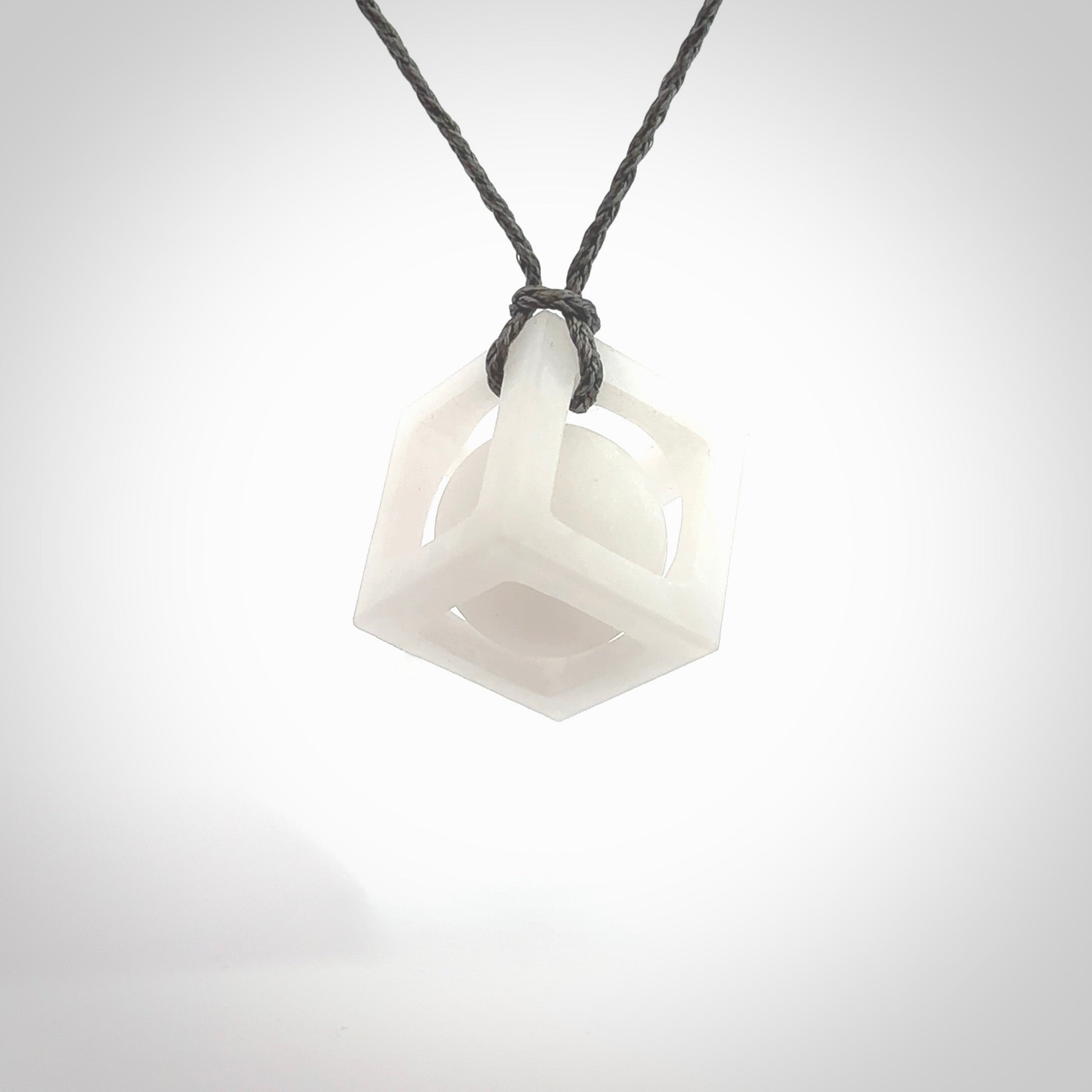 A hand carved medium sized white nephrite Jade square box with ball inside necklace. The cord is grey and adjustable in length. A medium sized hand made cube/box with ball necklace in white nephrite Jade stone. One off work of art to wear.