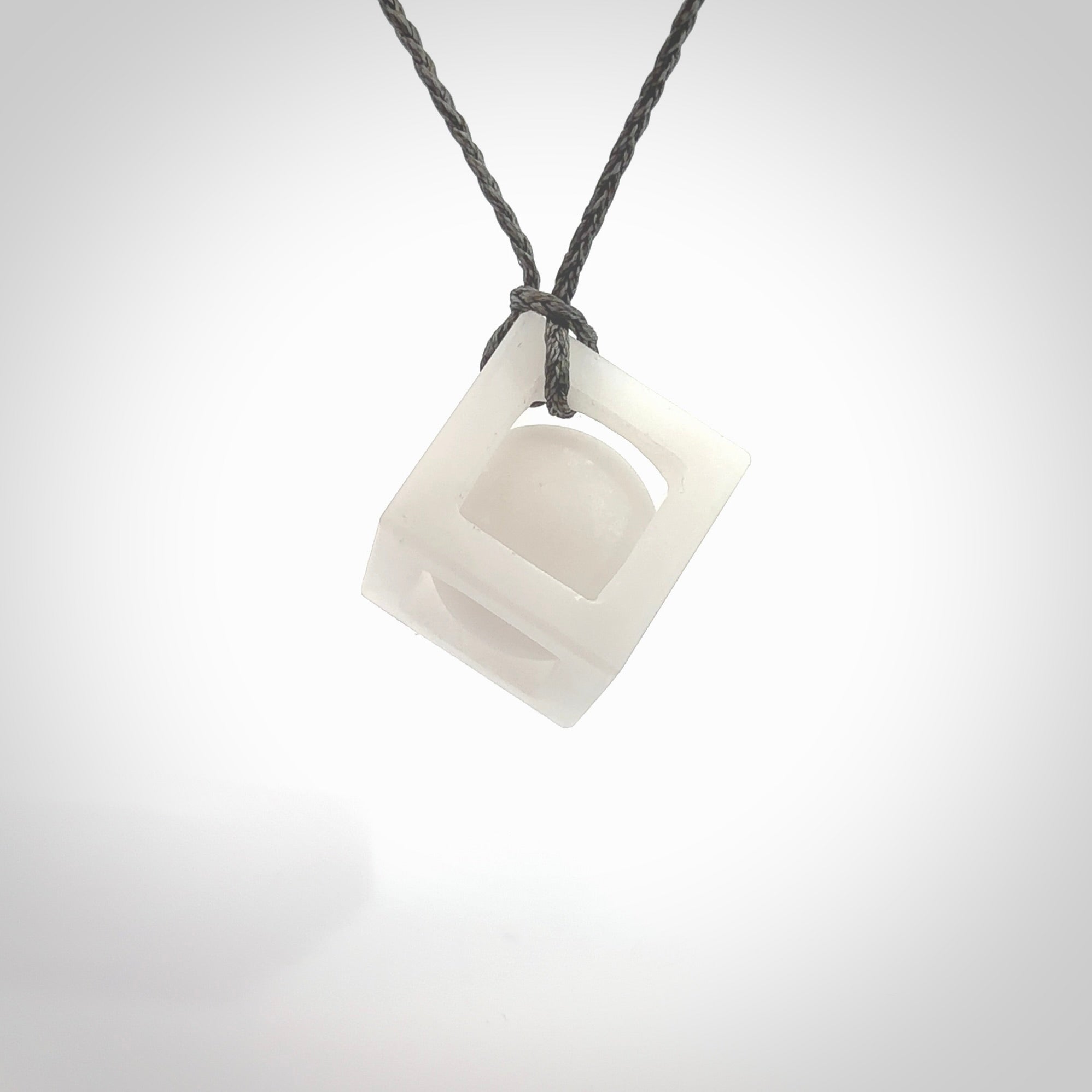 A hand carved medium sized white nephrite Jade square box with ball inside necklace. The cord is grey and adjustable in length. A medium sized hand made cube/box with ball necklace in white nephrite Jade stone. One off work of art to wear.