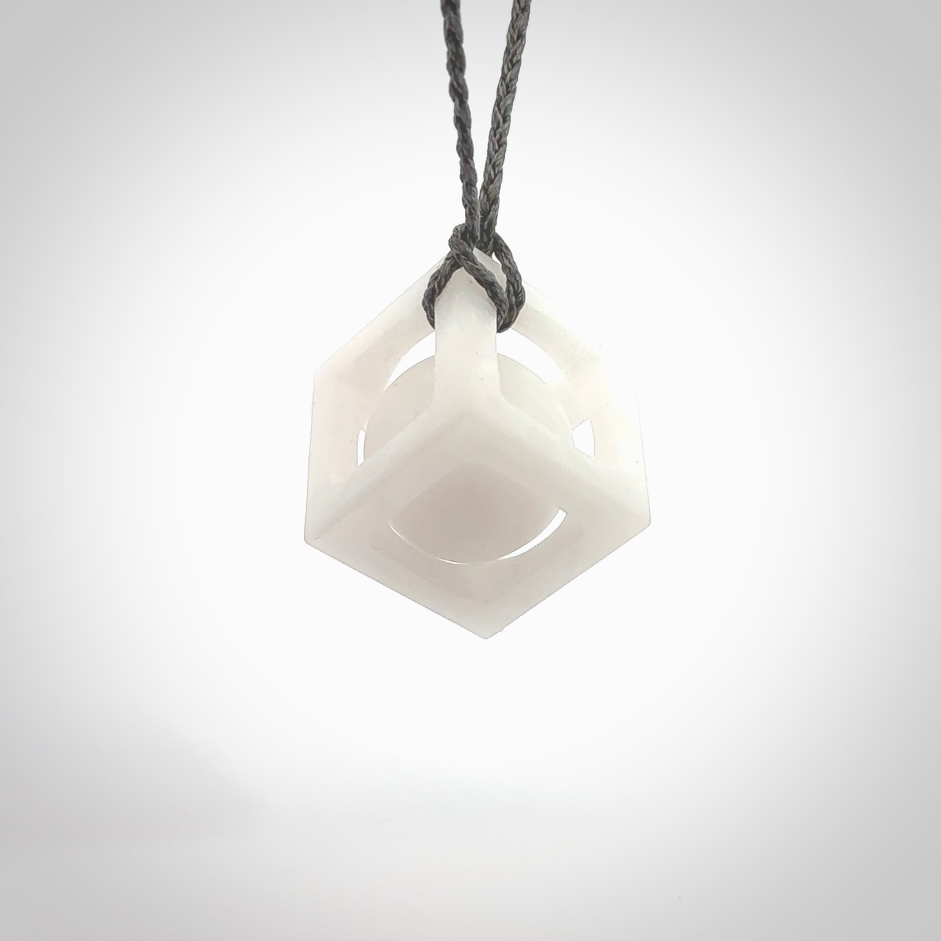 A hand carved medium sized white nephrite Jade square box with ball inside necklace. The cord is grey and adjustable in length. A medium sized hand made cube/box with ball necklace in white nephrite Jade stone. One off work of art to wear.