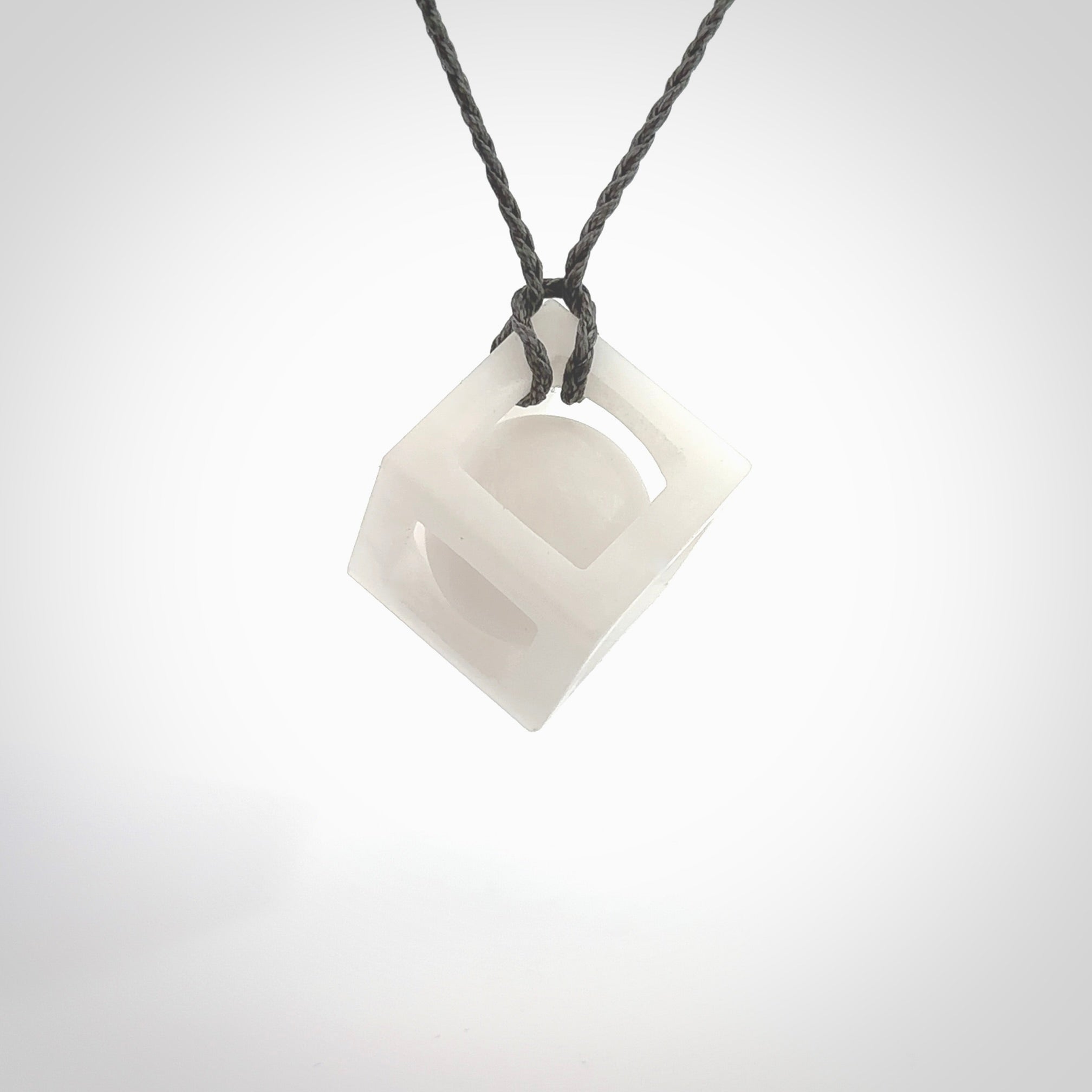 A hand carved medium sized white nephrite Jade square box with ball inside necklace. The cord is grey and adjustable in length. A medium sized hand made cube/box with ball necklace in white nephrite Jade stone. One off work of art to wear.