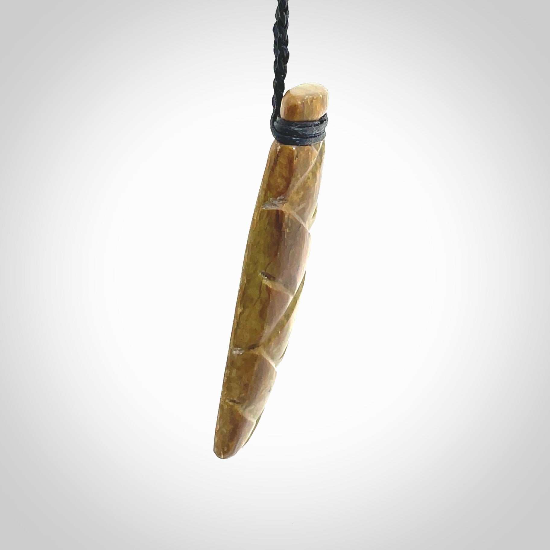 This picture shows a toki pendant carved with a woven front face and a flat back. It is made from a piece of rare New Zealand Flower Jade by our artist and carver Ana Krakosky. The cord is black and is length adjustable.