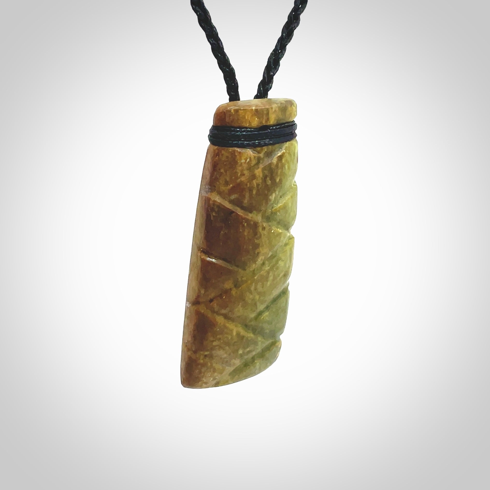 This picture shows a toki pendant carved with a woven front face and a flat back. It is made from a piece of rare New Zealand Flower Jade by our artist and carver Ana Krakosky. The cord is black and is length adjustable.