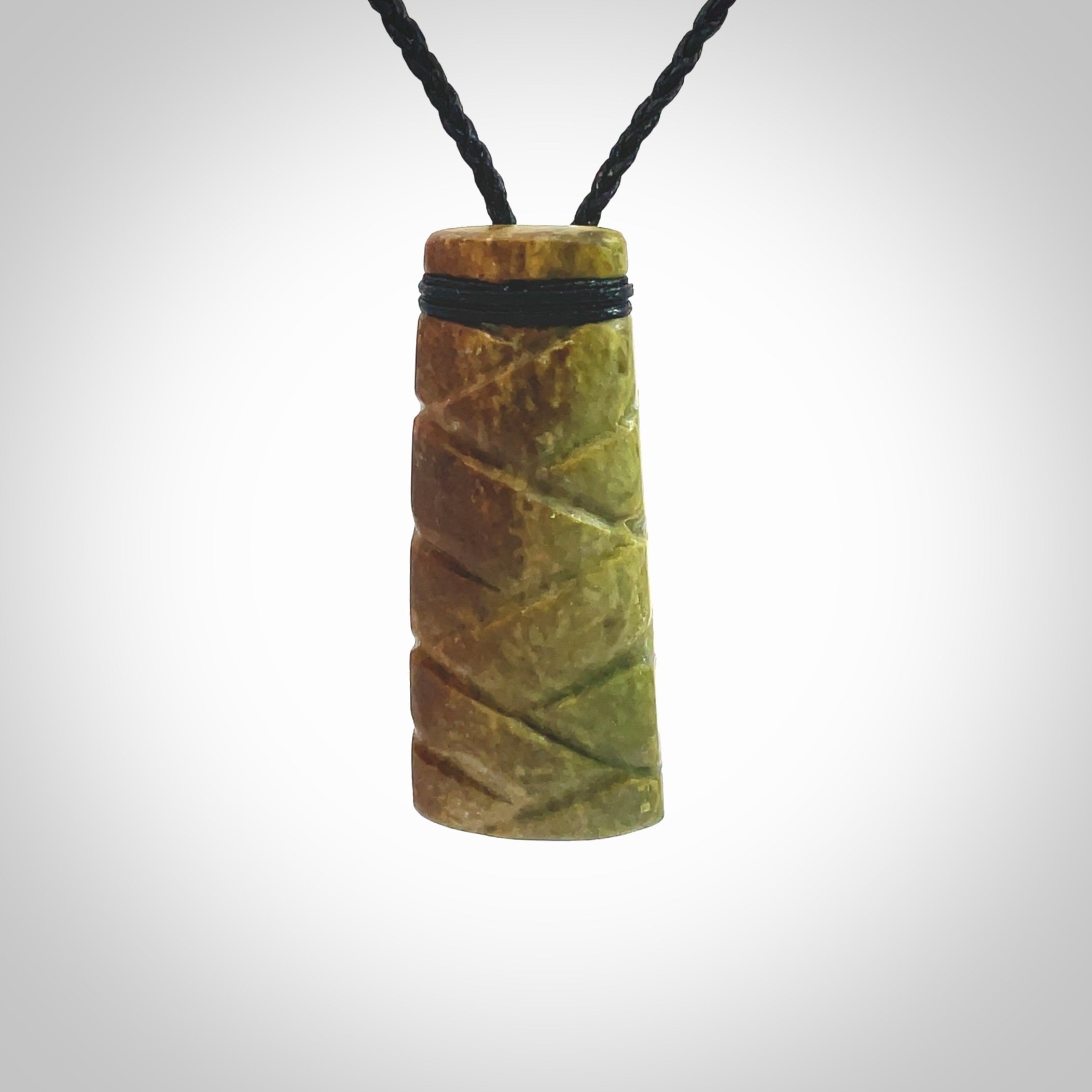 This picture shows a toki pendant carved with a woven front face and a flat back. It is made from a piece of rare New Zealand Flower Jade by our artist and carver Ana Krakosky. The cord is black and is length adjustable.