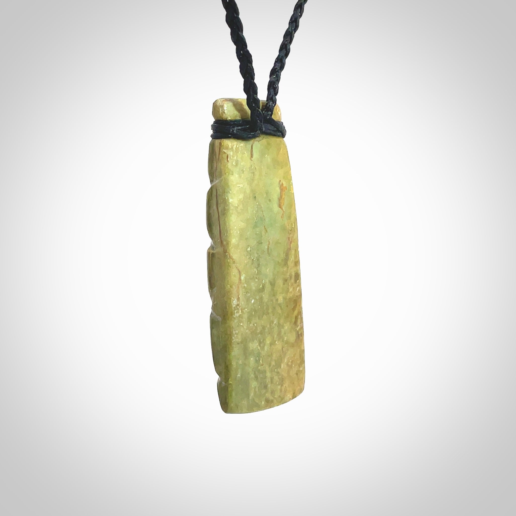 This picture shows a toki pendant carved with a woven front face and a flat back. It is made from a piece of rare New Zealand Flower Jade by our artist and carver Ana Krakosky. The cord is black and is length adjustable.