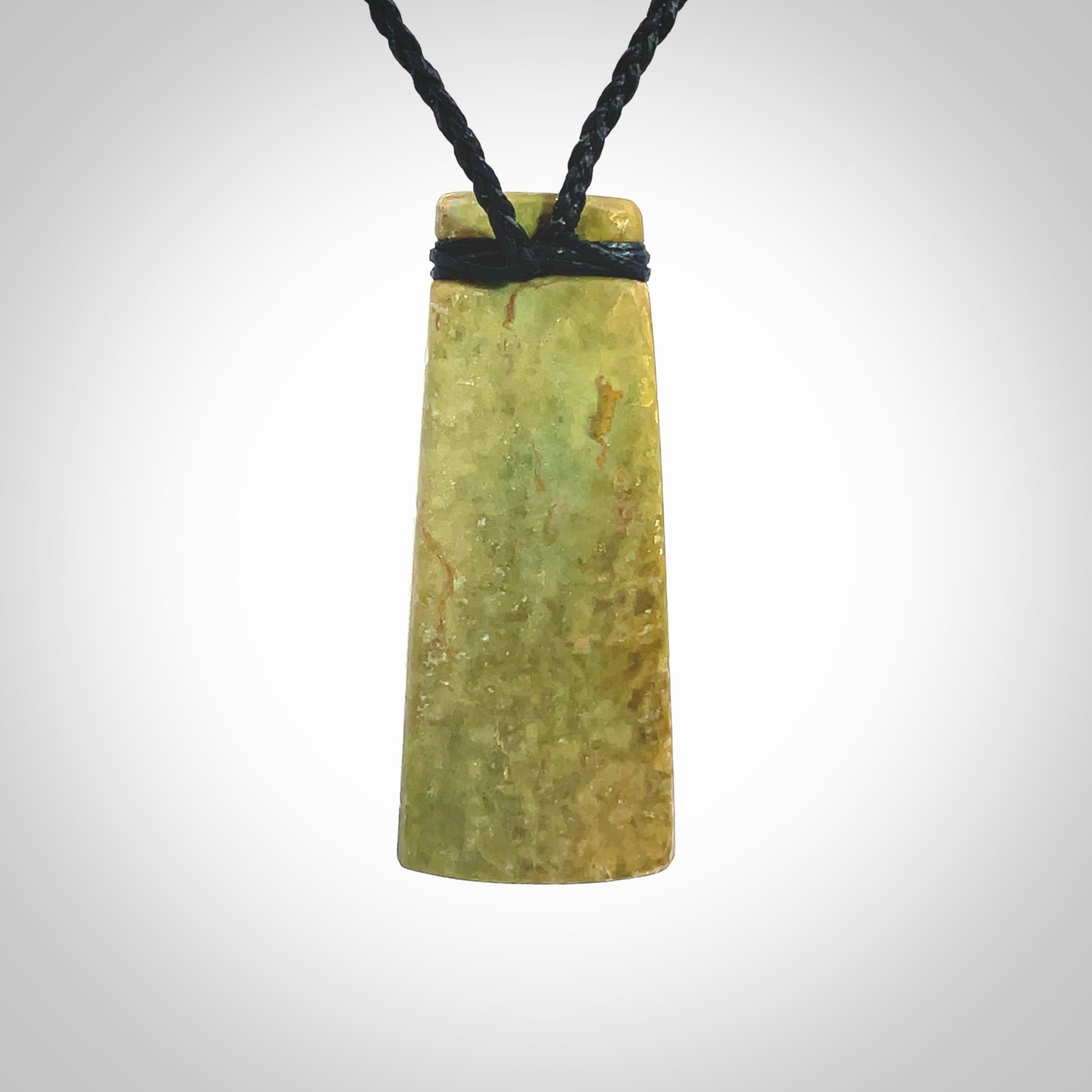 This picture shows a toki pendant carved with a woven front face and a flat back. It is made from a piece of rare New Zealand Flower Jade by our artist and carver Ana Krakosky. The cord is black and is length adjustable.