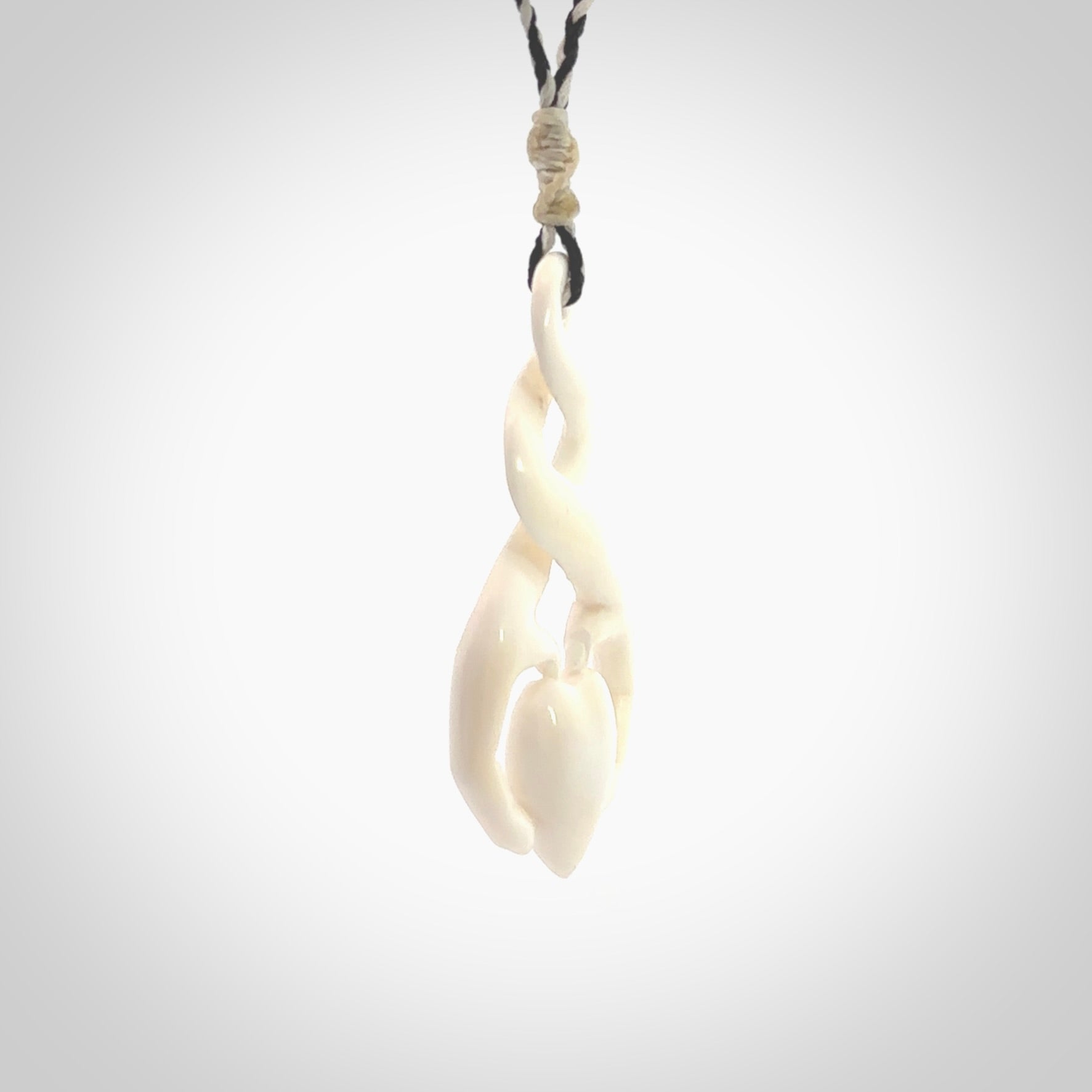 A hand carved intricate twist with heart in finger tips design pendant from Bone. The cord is black and ice white and adjustable in length. Medium hand made twist with heart in hand necklace. One only pendant.