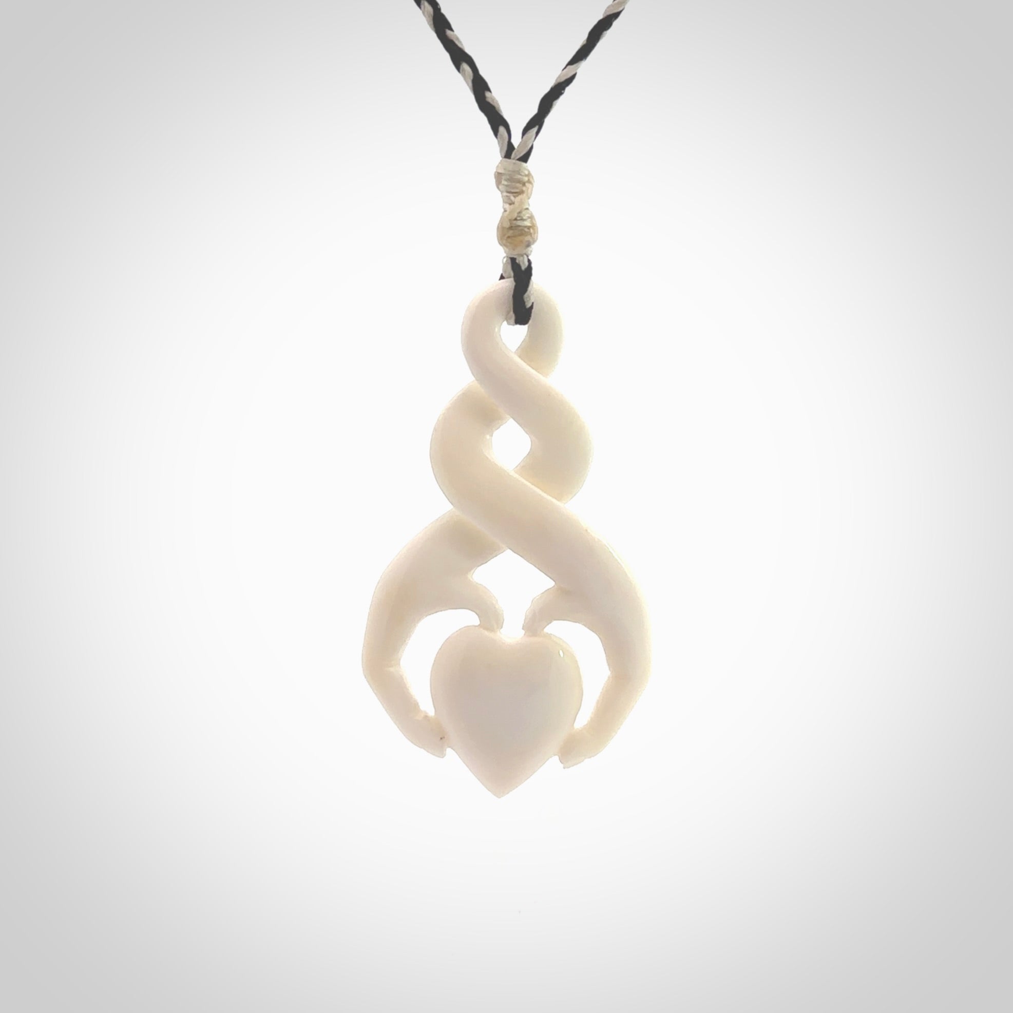 A hand carved intricate twist with heart in finger tips design pendant from Bone. The cord is black and ice white and adjustable in length. Medium hand made twist with heart in hand necklace. One only pendant.