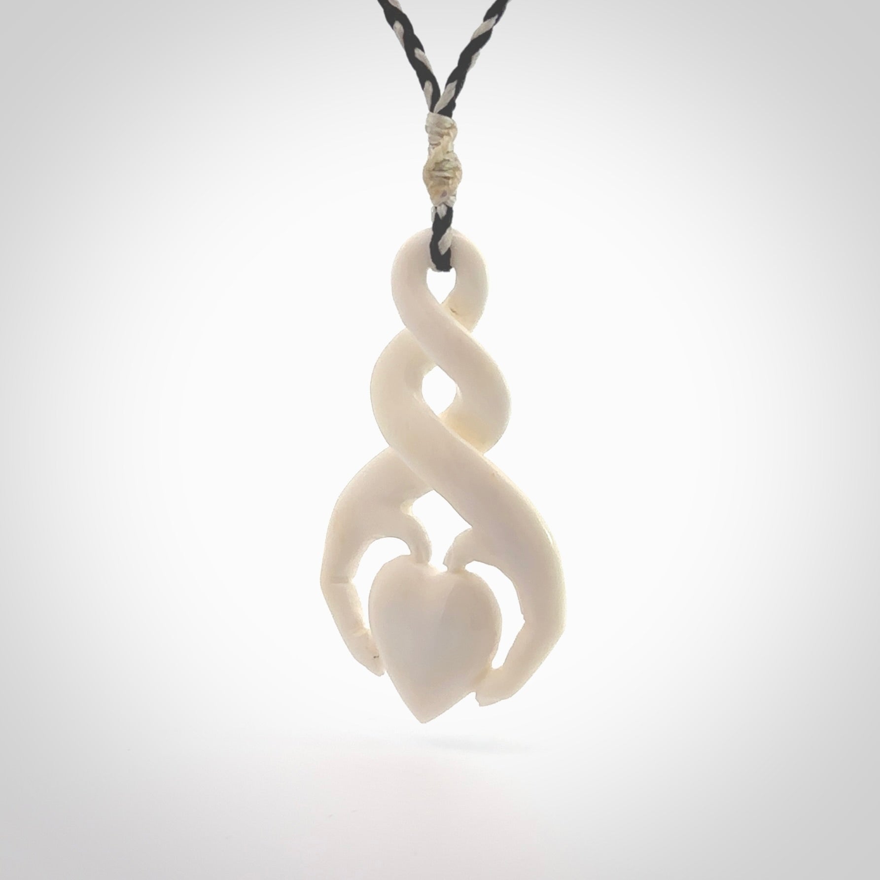 A hand carved intricate twist with heart in finger tips design pendant from Bone. The cord is black and ice white and adjustable in length. Medium hand made twist with heart in hand necklace. One only pendant.