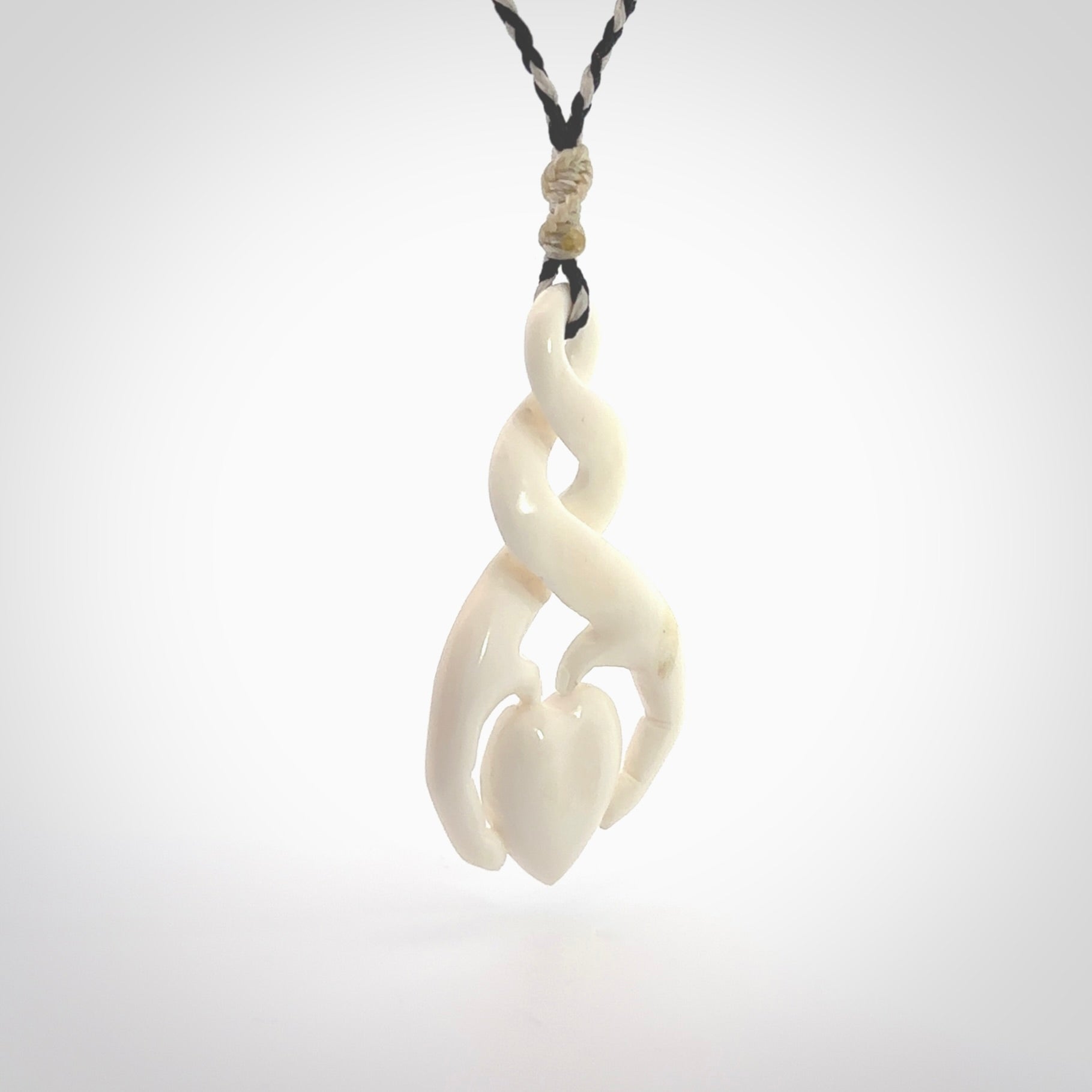 A hand carved intricate twist with heart in finger tips design pendant from Bone. The cord is black and ice white and adjustable in length. Medium hand made twist with heart in hand necklace. One only pendant.