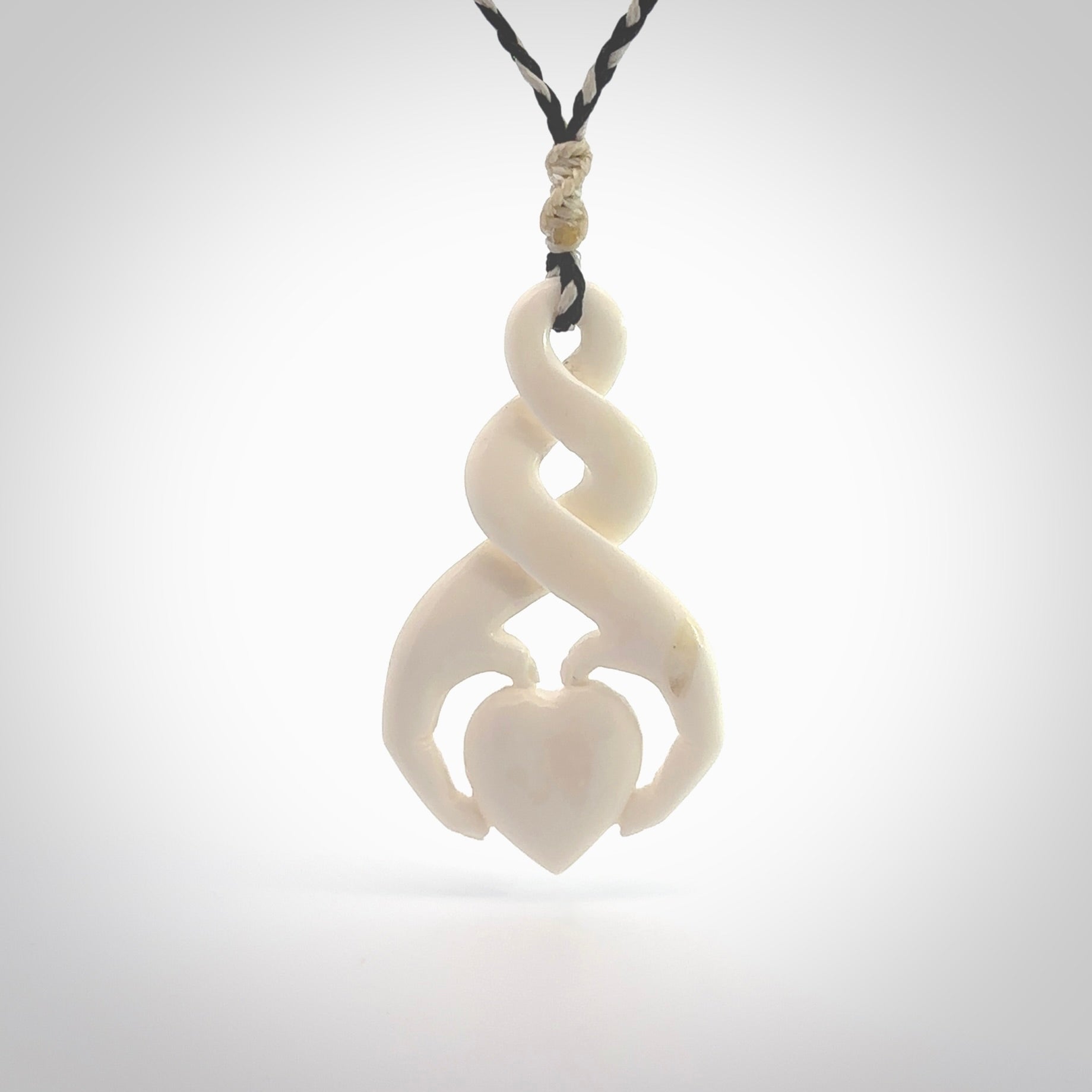 A hand carved intricate twist with heart in finger tips design pendant from Bone. The cord is black and ice white and adjustable in length. Medium hand made twist with heart in hand necklace. One only pendant.