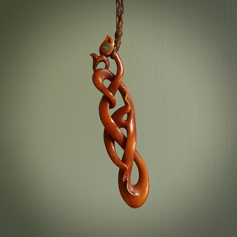 A one off beautiful piece of carved art. We have called this Wrap Around, it was hand carved for us by Yuri Terenyi and is a manaia with twist design pendant. This is a wonderful ethnic bone pendant designed to be worn. It has been stained by a homemade tea dye in a bright gingery brown colour and we have hand plaited an adjustable cord in wapiti and ginger nut colours.