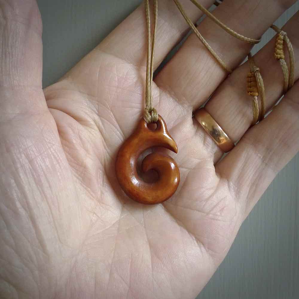 Stained natural cow bone hook with koru pendant. Hand carved by Yuri Terenyi in New Zealand. Koru design pendant for sale online. Stained bone koru necklace with adjustable brown cord. Free delivery worldwide.