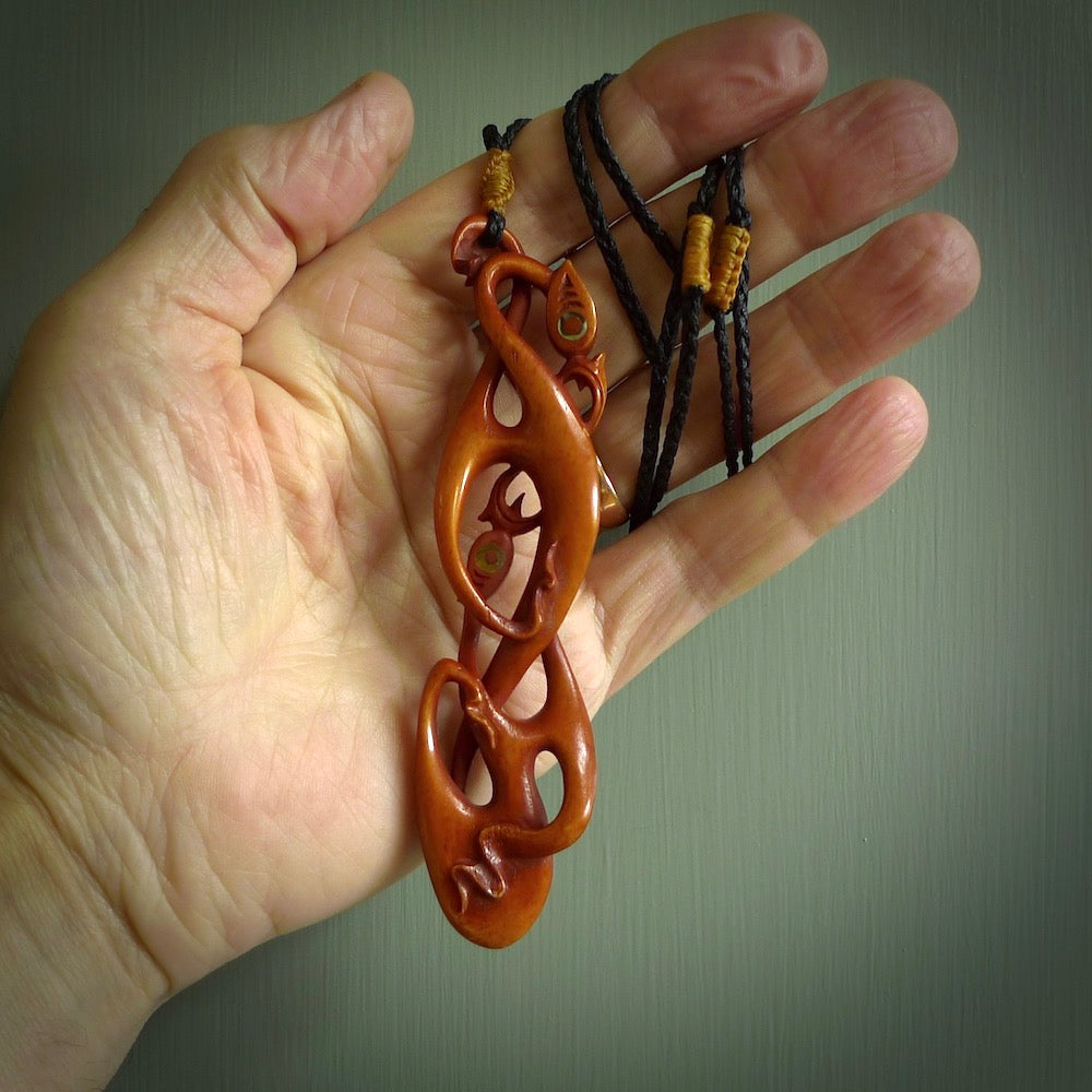 A one off beautiful piece of carved art. Hand carved for us by Yuri Terenyi and is a double manaia pendant. This is a wonderful ethnic bone pendant designed to be worn. It has been stained by a homemade tea dye in a bright gingery brown colour and we have hand plaited an adjustable cord in black with a burnt gold floret popper.