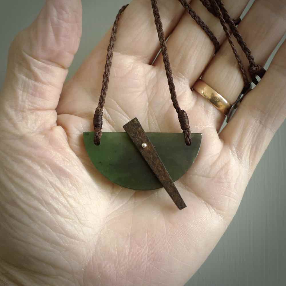 This piece is a contemporary shield pendant carved from jade from New Zealand. It is a deep green colour. The cord is brown and is length adjustable. Hand made with Australian Black Jade and Jade.