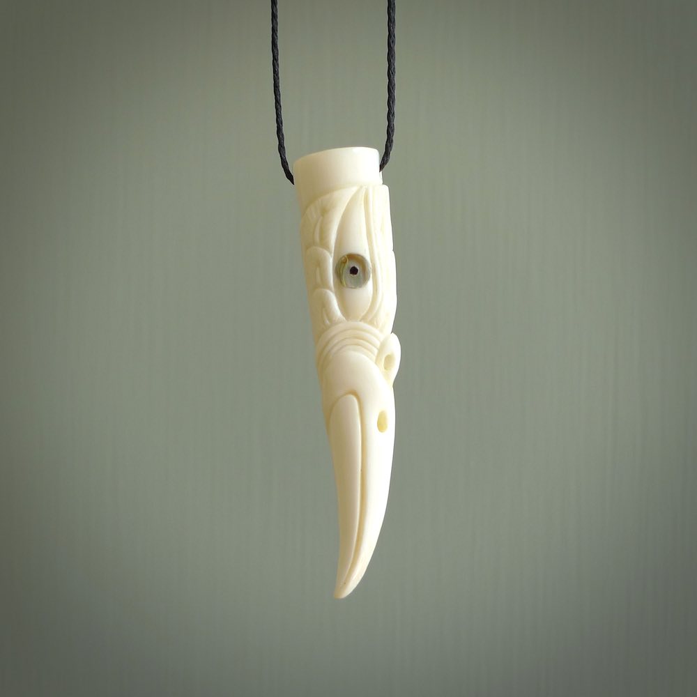 A mythical bird head hand carved from bone with Paua shell eyes. This is a one only bird head with long beak necklace hand made from natural bone with paua shell eyes. This bird head has engravings and is a magnificent piece of art to wear. It is delivered on a black adjustable cord.