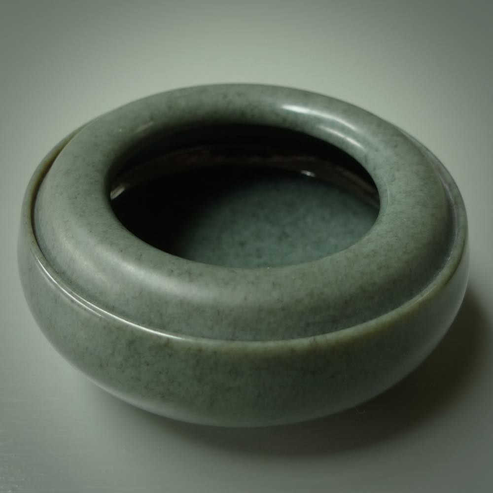 This photo shows a hand carved, Wyoming 'Sage' Nephrite Jade bowl sculpture. This 3.5 inch bowl carved from extremely fine-grained Sage. With Wyoming Black Jade and Sterling Silver, high domed centre grip. This hand crafted work of art was hand made by award winning New Zealand carver Donn Salt.