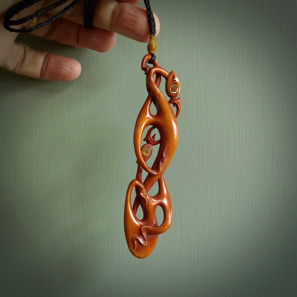 A one off beautiful piece of carved art. Hand carved for us by Yuri Terenyi and is a double manaia pendant. This is a wonderful ethnic bone pendant designed to be worn. It has been stained by a homemade tea dye in a bright gingery brown colour and we have hand plaited an adjustable cord in black with a burnt gold floret popper.