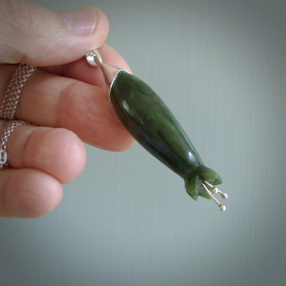 A photo of a harakeke, or flax flower, carved from a colourful piece of New Zealand flower jade. The cap and stamens are made from Sterling Silver and the cord is an Olive braid which is length adjustable.