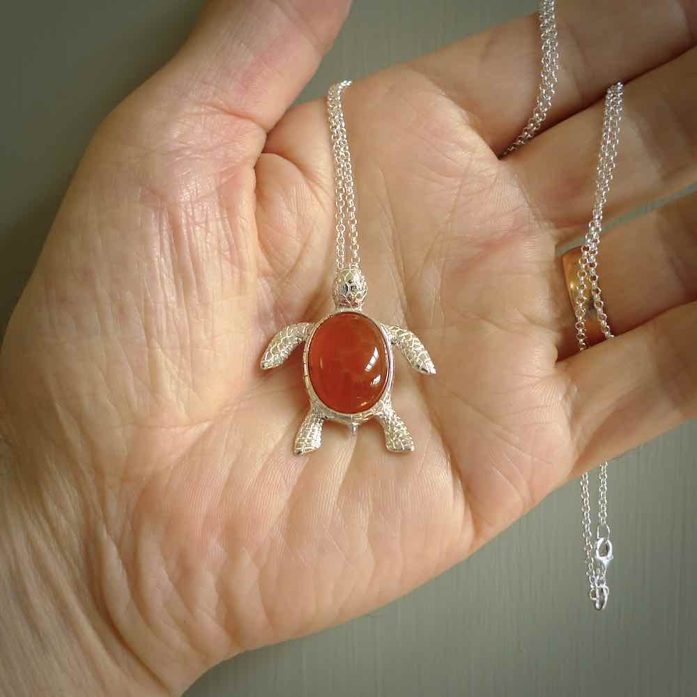 Fire Agate stone turtle in Sterling silver engraved casing. Hand carved jewellery made by NZ Pacific and for sale online. Moana, Ocean, jewellery hand carved in fire agate and Sterling Silver turtle necklace.