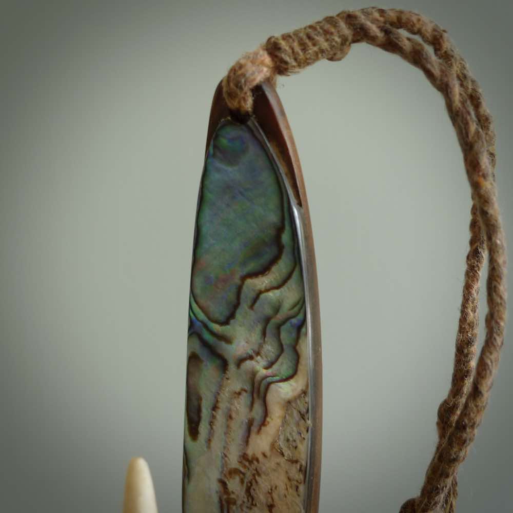 This picture shows a small sculptural hook called a pā kahawai. It is carved from whale bone, paua shell and wood, and is a colourful blue grey colour. It is shown on a stand made from argillite stone and is held in a brass cradle. One only, free shipping worldwide.