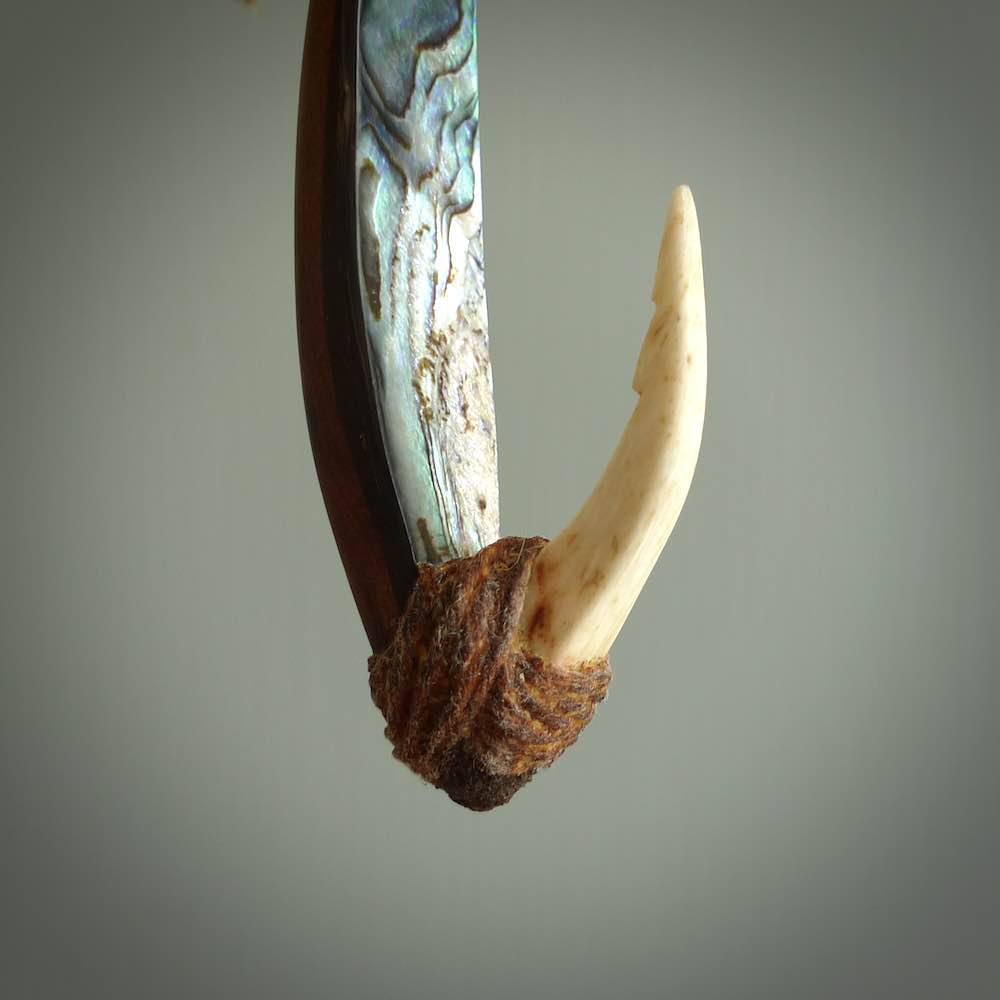 This picture shows a small sculptural hook called a pā kahawai. It is carved from whale bone, paua shell and wood, and is a colourful blue grey colour. It is shown on a stand made from argillite stone and is held in a brass cradle. One only, free shipping worldwide.