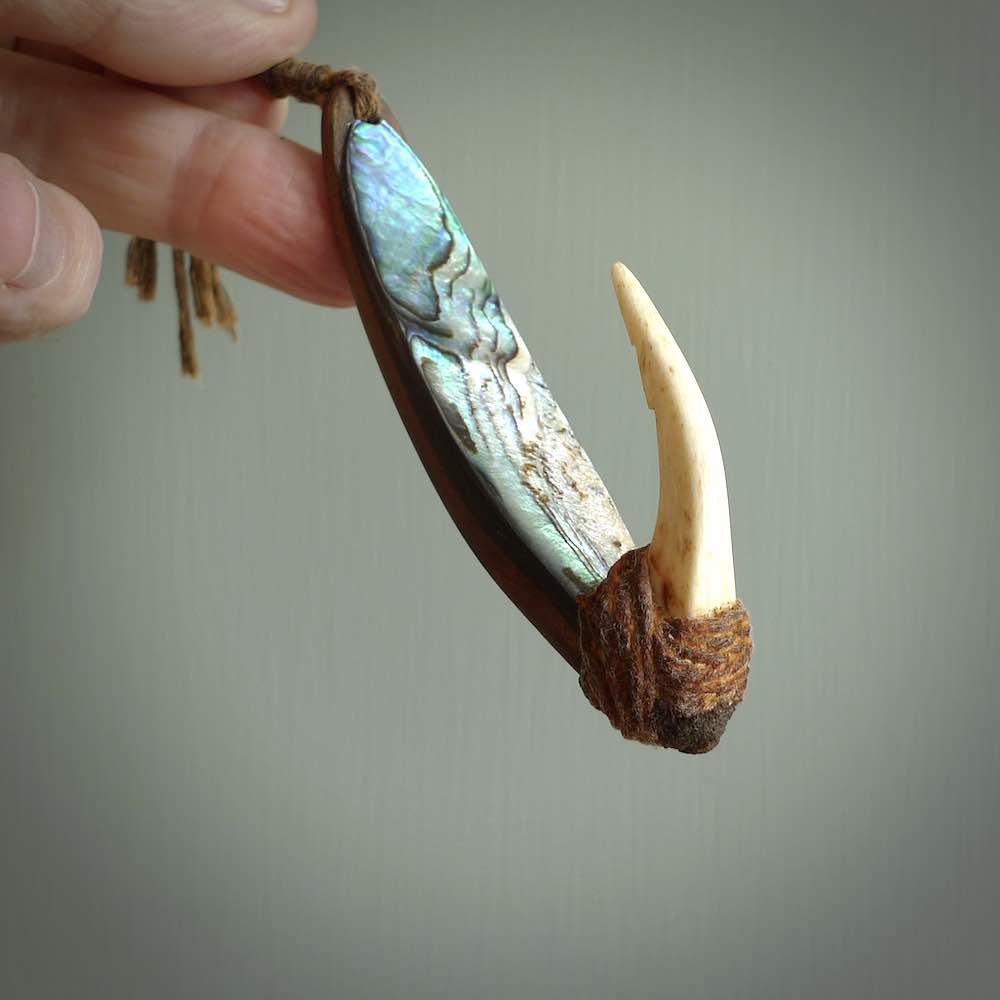 This picture shows a small sculptural hook called a pā kahawai. It is carved from whale bone, paua shell and wood, and is a colourful blue grey colour. It is shown on a stand made from argillite stone and is held in a brass cradle. One only, free shipping worldwide.