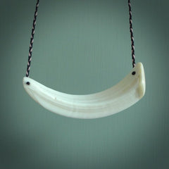 This photo shows a pendant we carved from boars tusk. It is a Blue Whale carved lengthwise into the tusk. This piece is suspended from a hand plaited necklace cord in Black and Pink. This pendant in 100% hand made.